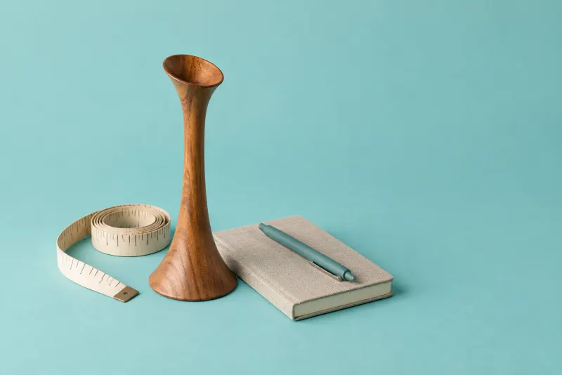 A wooden Pinard fetoscope, a measuring tape and a notebook on a teal backdrop